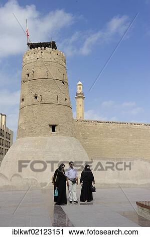 Stock Image - Arab man with his wives standing in front of the tower of the fort in Dubai, Dubai museum, United Arab Emirates, Arabia, Arabian Peninsula, Asia. Fotosearch