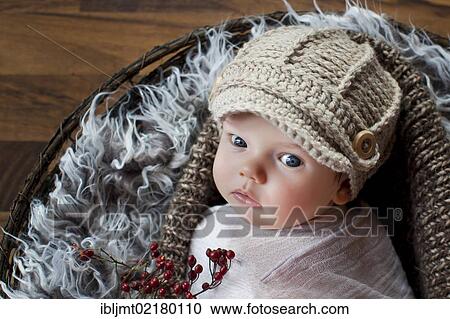 Stock Image - Baby, 2 months, wearing a knitted cap and lying in a basket. Fotosearch