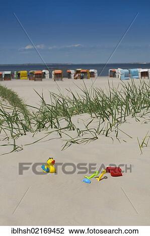 Colorful children's toys, bucket, spades and duck, in the sand on the beach of Norden, beach chairs against the blue sky at back, Norddeich Mole, Lower Saxony, Germany, Europe View Large Photo Image Stock Image - Colorful children's toys, bucket, spades and duck, in the sand on the beach of Norden, beach chairs against the blue sky at back, Norddeich Mole, Lower Saxony, Germany, Europe. Fotosearch