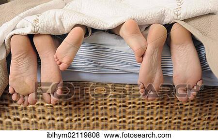 Stock Photo - Family with a child, feet looking out from under a blanket. Fotosearch