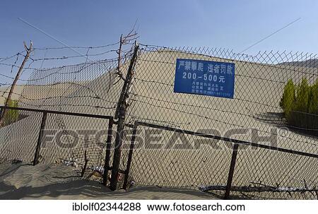 Stock Photo - Fence resticting access to sand dunes of the Gobi Desert, sign with entrance fees and threat of penalties for unauthorised entrance, near Dunhuang, Silk Road, Gansu, China, Asia. Fotosearch