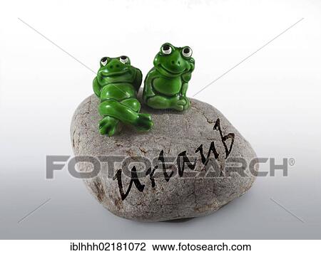 Stock Image - Frog figures on a stone with the inscription Urlaub, German for Holidays. Fotosearch
