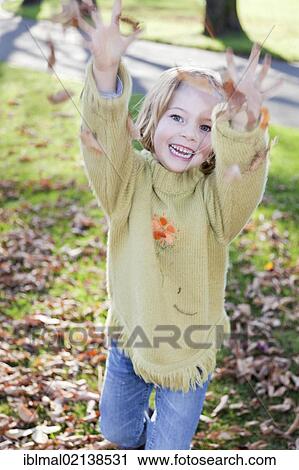 Stock Image - Girl, 6, throwing leaves in autumn. Fotosearch