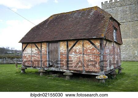 Stock Image - Granary with bricks and rotten wooden door, supported by mushroom-shaped staddle stones, old barn at Cowdray, Midhurst, West Sussex, England, United Kingdom, Europe. Fotosearch