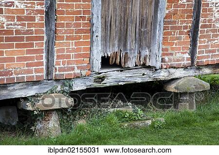 Stock Image - Granary with bricks and rotten wooden door, supported by mushroom-shaped staddle stones, old barn at Cowdray, Midhurst, West Sussex, England, United Kingdom, Europe. Fotosearch