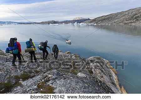 Stock Image - Group of hikers approaching an expected motorboat, icebergs near Tiniteqilaaq, Ammassalik Peninsula, Sermilik Fjord, East Greenland, Greenland, North America. Fotosearch