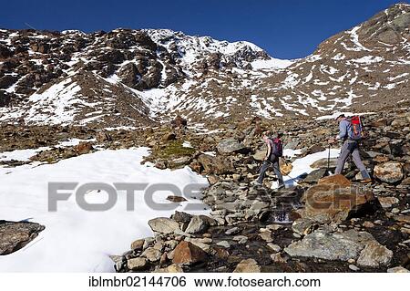 Stock Photograph - Hikers ascending Hintere Eggenspitze Mountain in Ulten Valley above Gruensee Lake, looking towards Weissbrunnspitze Mountain, Alto Adige, Italy, Europe. Fotosearch