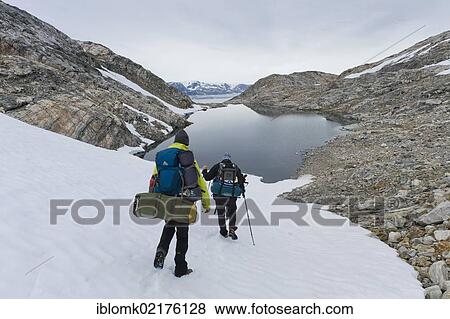 Stock Photo - Hikers with backpacks on a field of snow, lake, at Sermilik Fjord, Ammassalik Peninsula, East Greenland, Greenland, North America. Fotosearch