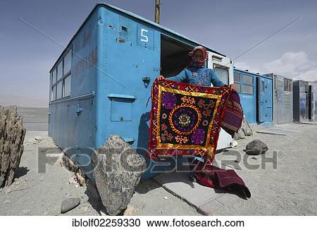 Stock Image - Kazakh woman showing a hand-woven, embroidered wall carpet, simple blue containers, house boxes, storage containers, shops of the Kazakhs in the Kongur Mountains, Silk Road, Pamir, Xinjiang, China, Asia. Fotosearch