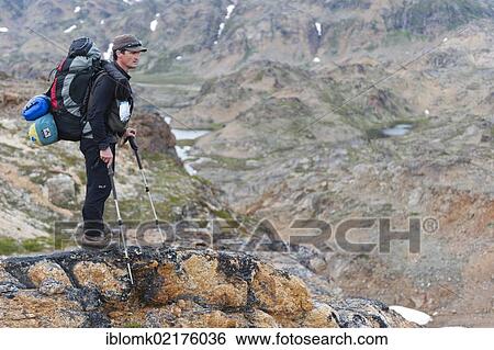 Stock Photograph - Leader of a group of hikers with a backpack and a rifle, Ammassalik Peninsula, East Greenland, Greenland, North America. Fotosearch