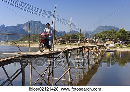 Stock Photo - Moped rider crossing the bamboo bridge over the Nam Song River, karst mountains, Vang Vieng, Vientiane, Laos, Indochina, Asia. Fotosearch