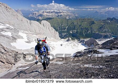 Stock Photo - Mountain climber ascending Marmolada Mountain on the Westgrat climbing route, view towards Sella Mountain, the Heiligkreuzkofelgruppe range, Fedaia Pass and Lake Fedaia, Trentino, Dolomites, Italy, Europe. Fotosearch