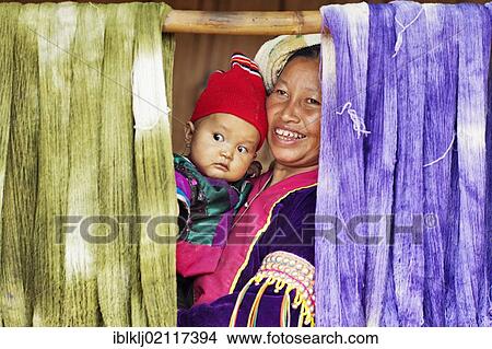 Picture - Palong mother and child looking out from between died thread hanging out to dry in Norlae village, northern Thailand, Asia. Fotosearch