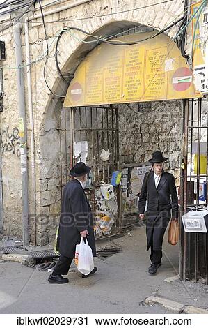 Stock Image - Sign prohibiting the entry of non-Orthodox Jews in a residential housing estate, with two Orthodox Jews passing through the gateway, in the district of Me'a She'arim or Mea Shearim, Jerusalem, Israel, Middle East, Asia. Fotosearch