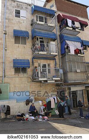 Stock Image - Street scene, woman selling clothes in the street, residential houses with balconies that are being used, in front of the Mahane Yehuda Market, Jerusalem, Israel, Middle East, Asia. Fotosearch