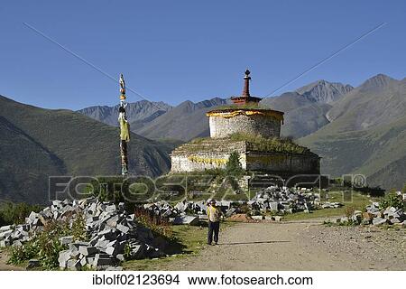 Picture - Tibetan Buddhism, Tibetan man holding a prayer wheel in front of a stupa, chorten, in the mountains of Reting Monastery, Mount Gangi Rarwa, Himalayas, Lhundrup district, Central Tibet, China, Asia. Fotosearch
