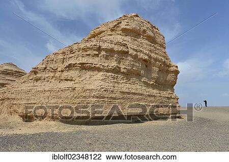 Stock Image - Tourist standing in a dry stony desert landscape with rock formations, historic Silk Road, Yumen Pass, Yadan National Park, Gansu, China, Asia. Fotosearch