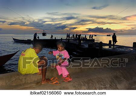 Two Papuan children eating on the quay walls of the fishing port at sunset, Kota Biak, Biak Island, Irian Jaya, Indonesia, Southeast Asia, Asia View Large Photo Image Stock Image - Two Papuan children eating on the quay walls of the fishing port at sunset, Kota Biak, Biak Island, Irian Jaya, Indonesia, Southeast Asia, Asia. Fotosearch