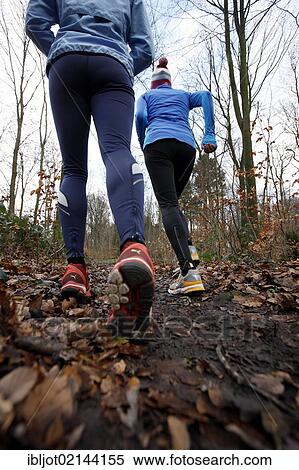 Stock Photography - Two young women jogging through a forest in winter, wearing wind and waterproof performance apparel. Fotosearch