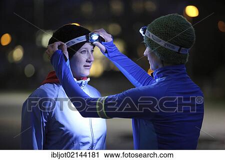 Two young women preparing to go jogging at dusk in winter, putting on reflector strips and LED headlamps, wearing reflective wind and waterproof performance apparel View Large Photo Image Stock Image - Two young women preparing to go jogging at dusk in winter, putting on reflector strips and LED headlamps, wearing reflective wind and waterproof performance apparel. Fotosearch