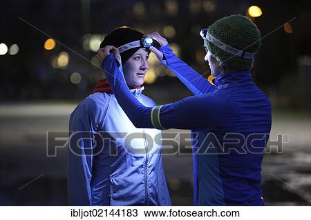Two young women preparing to go jogging at dusk in winter, putting on reflector strips and LED headlamps, wearing reflective wind and waterproof performance apparel View Large Photo Image Stock Image - Two young women preparing to go jogging at dusk in winter, putting on reflector strips and LED headlamps, wearing reflective wind and waterproof performance apparel. Fotosearch