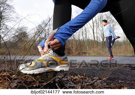 Two young women tying their shoes and stretching before jogging in winter, wearing wind and waterproof performance apparel View Large Photo Image Stock Photo - Two young women tying their shoes and stretching before jogging in winter, wearing wind and waterproof performance apparel. Fotosearch