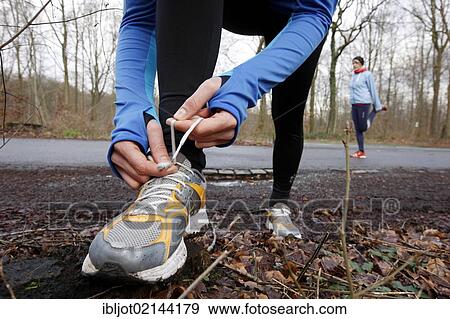 Two young women tying their shoes and stretching before jogging in winter, wearing wind and waterproof performance apparel View Large Photo Image Stock Photo - Two young women tying their shoes and stretching before jogging in winter, wearing wind and waterproof performance apparel. Fotosearch