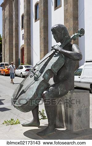 Village square with a bronze sculpture of a cello player, Homenaje a la Musica by A L Benitez in the historic centre of Agueimes, Gran Canaria, Canary Islands, Spain, Europe View Large Photo Image Stock Image - Village square with a bronze sculpture of a cello player, Homenaje a la Musica by A L Benitez in the historic centre of Agueimes, Gran Canaria, Canary Islands, Spain, Europe. Fotosearch