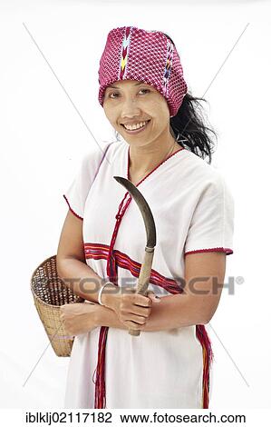 Stock Image - Woman wearing the traditional dress for an unmarried Karen woman and holding a knife used for harvesting rice, Thailand, Asia. Fotosearch