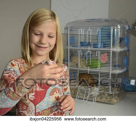 Stock Photograph - Blond Swedish girl, nine years old, holding newborn hamsters, in front of a hamster cage, Ystad, Sweden, Europe. Fotosearch