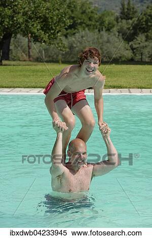 Stock Photography - Teenage boy standing on his father's shoulders in a swimming pool. Fotosearch