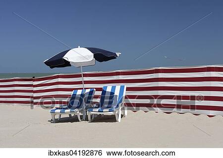 Stock Photograph - Two empty sun-beds behind a windbreak, beach on the North Sea, De Haan's Belgian Coast, West Flanders, Belgium, Europe. Fotosearch