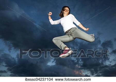 Picture - Young woman, 19 years old, jumping, in mid-air, against the evening sky. Fotosearch