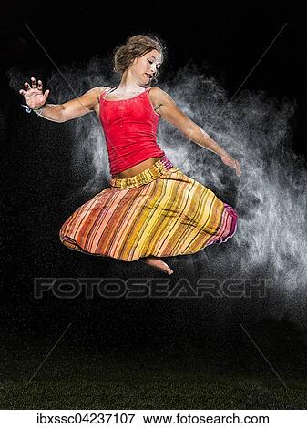 Stock Photo - Young woman, 19 years old, jumping, in mid-air with white dust, against the evening sky. Fotosearch