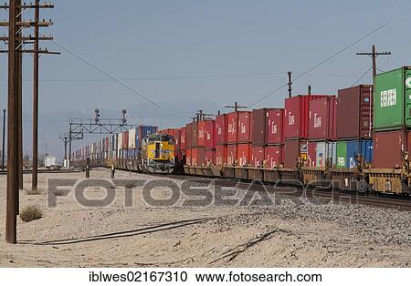 Stock Image - An eastbound Union Pacific freight train carrying shipping containers waits on a siding for a westbound train, also carrying shipping containers, to pass, Niland, California, USA, North America. Fotosearch