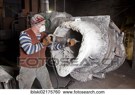 Stock Image - An employee of Luitpoldhuette AG, a foundry that specializes in the casting of engine blocks, motor parts and refrigeration compressors, cleaning a bucket for the smelting process, in Amberg, Bavaria, Germany, Europe. Fotosearch