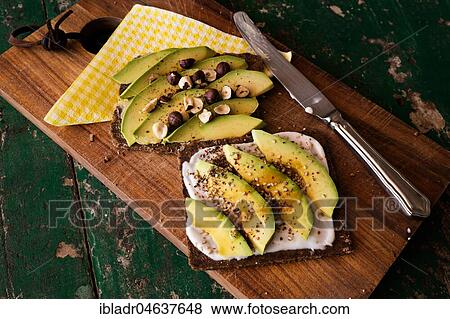Stock Photo - Black bread with curd cheese, avocado and nuts, food still-life, studio shot. Fotosearch