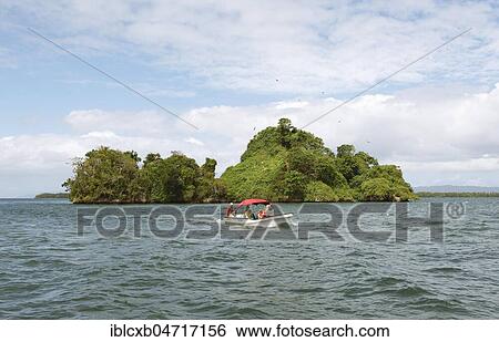 Stock Photograph - Cayo or rock island, frigate birds circling above, in front a motorboat, Los Haitises National Park, Samaná Province, Dominican Republic, Central America. Fotosearch