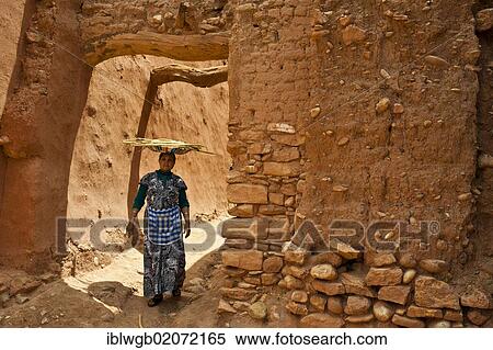 Stock Photography - Elderly Berber woman walking through an alleyway in a clay village, Ksar, carrying a bowl of twigs on her head, Tamdakht, southern Morocco, Morocco, Africa. Fotosearch