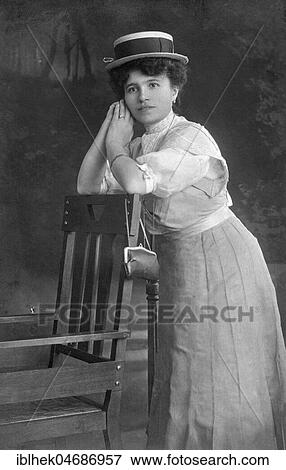 Stock Photo - Fashion, Woman with hat, dress and handbag leaning against a chair, 1910s, Germany, Europe. Fotosearch