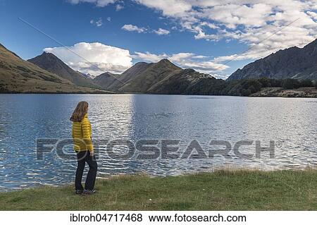 Stock Photo - Female hiker standing on the shore of Moke Lake near Queenstown, Lake with mountains, Otago, South Island, New Zealand, Oceania. Fotosearch