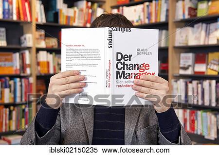 Stock Photography - Man holding a book in front of his face, in a bookstore in Regensburg, Bavaria, Germany, Europe. Fotosearch
