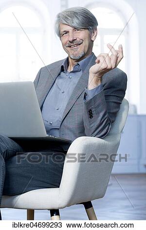 Stock Image - Man sits with laptop in his office chair. Fotosearch