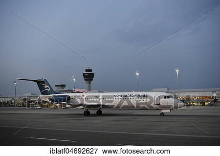 Stock Photo - Monte Airlines, Fokker, F100, taxiing in front of Terminal 1 with tower, at dusk, Munich Airport, Upper Bavaria, Bavaria, Germany, Europe. Fotosearch