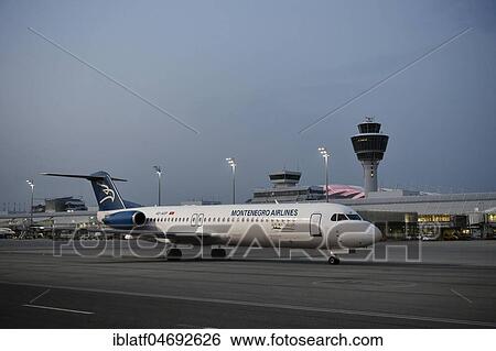 Stock Photograph - Monte Airlines, Fokker, F100, taxiing in front of Terminal 1 with tower, at dusk, Munich Airport, Upper Bavaria, Bavaria, Germany, Europe. Fotosearch