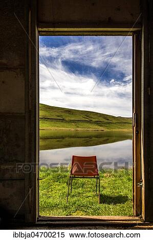Stock Photography - Orange chair standing in front of open window on a lake, Puy de dome department, Auvergne, France, Europe. Fotosearch