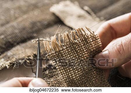 Stock Photography - Restoration atelier, hand processing linen patch with thread bridges over crack in lent scarf, Munich, Bavaria, Germany, Europe. Fotosearch