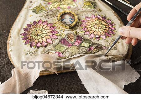 Picture - Restoration studio, restorer, hand holds fabric samples with tweezers on torn, artfully embroidered silk cloth, Munich, Bavaria, Germany, Europe. Fotosearch
