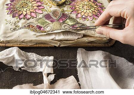 Stock Image - Restoration studio, restorer, hand checks artistically embroidered silk cloth torn open with tweezers, Munich, Bavaria, Germany, Europe. Fotosearch