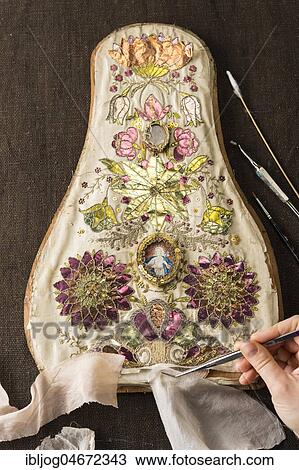 Stock Image - Restoration studio, restorer, hand holds fabric samples with tweezers on torn, artfully embroidered silk cloth, Munich, Bavaria, Germany, Europe. Fotosearch